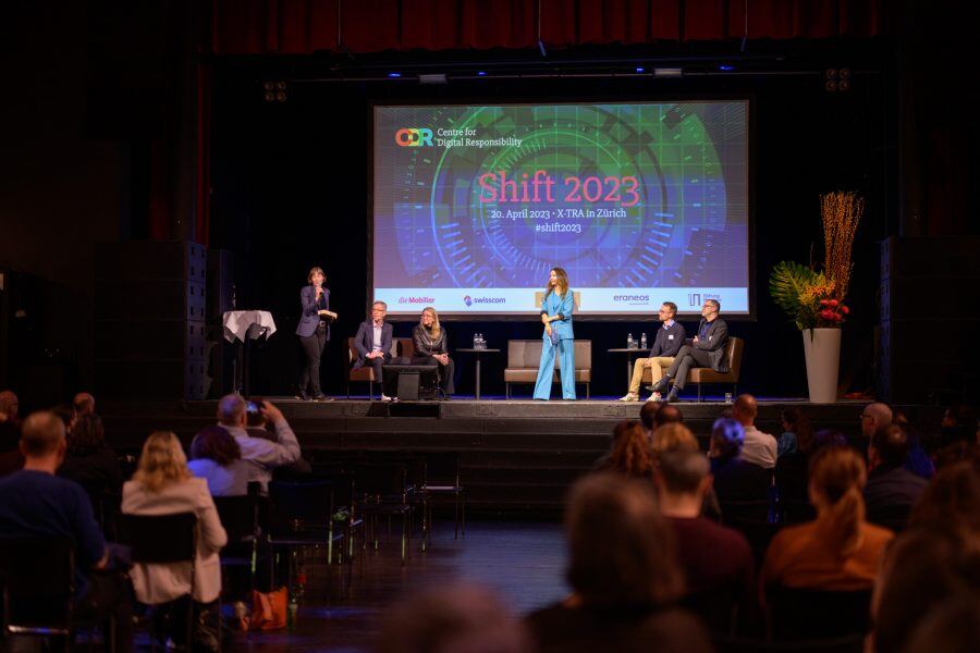 Die Intitiatorin und Gastgeberin der SHIFT Cornelia Diethelm (links am Mikrofon), das Abschluss-Panel und die Moderatorin Patrizia Laeri (Mitte). (c) Foto: Louis Rafael Rosenthal.